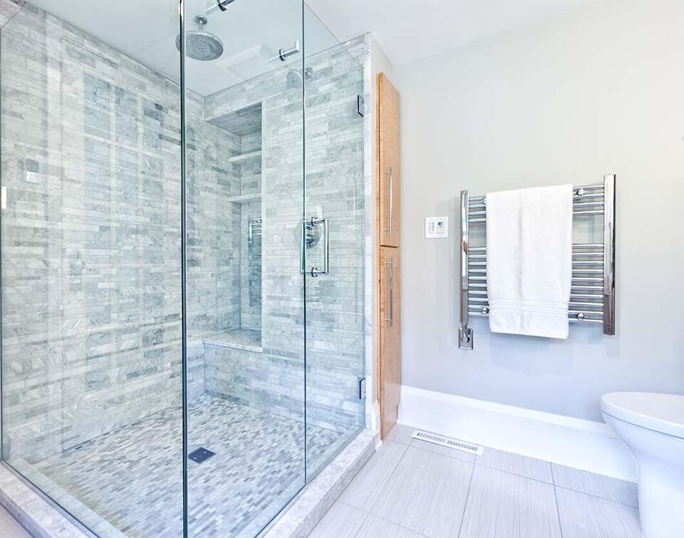 Frameless glass door and panel shower enclosure in a marble-tiled bathroom