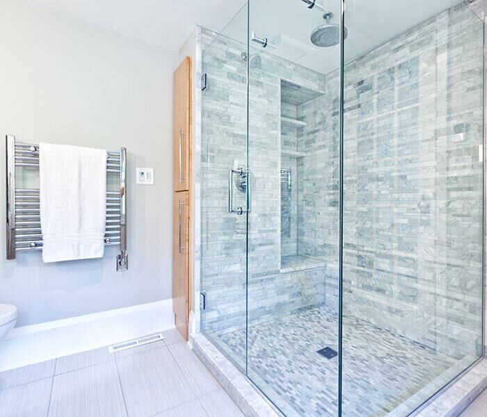 Frameless glass shower enclosure with clear panels beside a heated towel rack