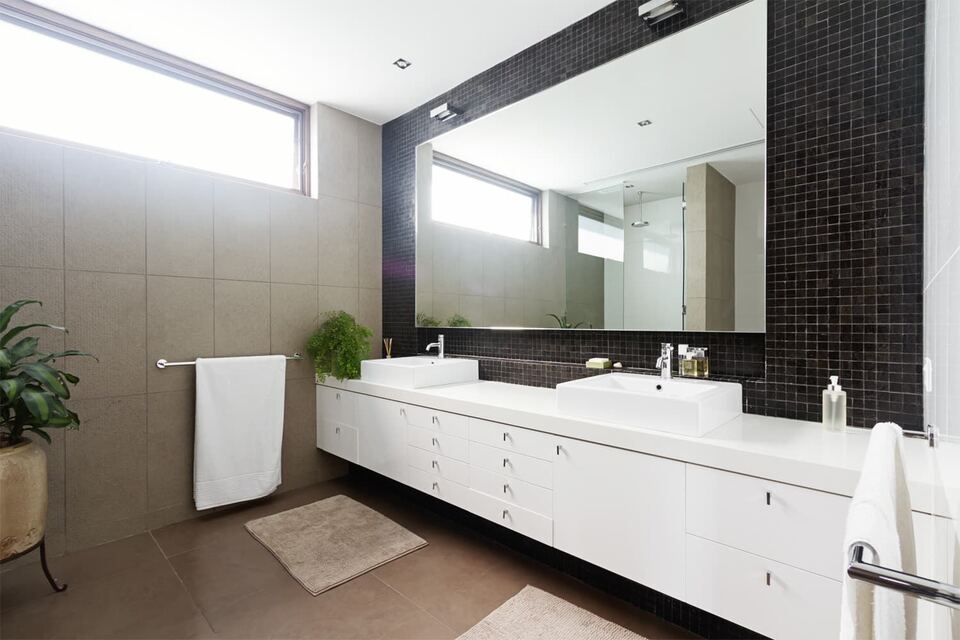 Wide frameless mirror above a floating double vanity with dark mosaic tile